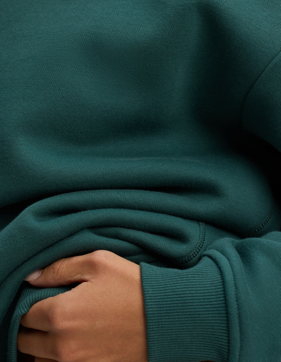Close-up of a person’s hand resting on the midsection of a dark green Women’s CityScape Crewneck sweatshirt.