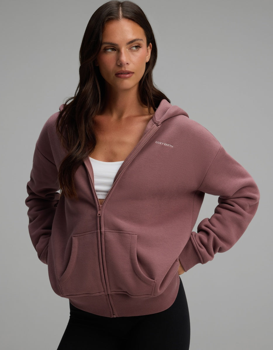 A woman wearing a mauve Cozy Earth Women’s CityScape Full-Zip Hoodie over a white crop top.|Color:Copper Rose