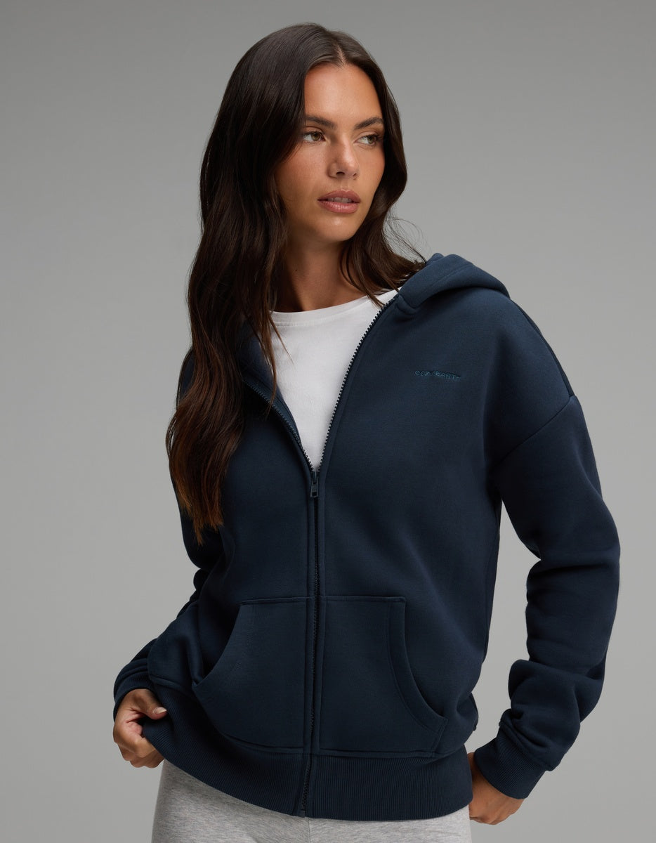 A woman wearing a dark navy blue Cozy Earth Women’s CityScape Full-Zip Hoodie over a white t-shirt.