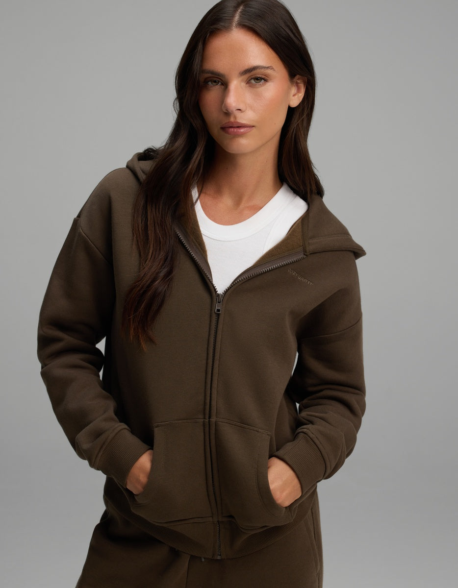 A woman wears a dark olive green Women’s CityScape Full-Zip Hoodie over a white crew-neck shirt.