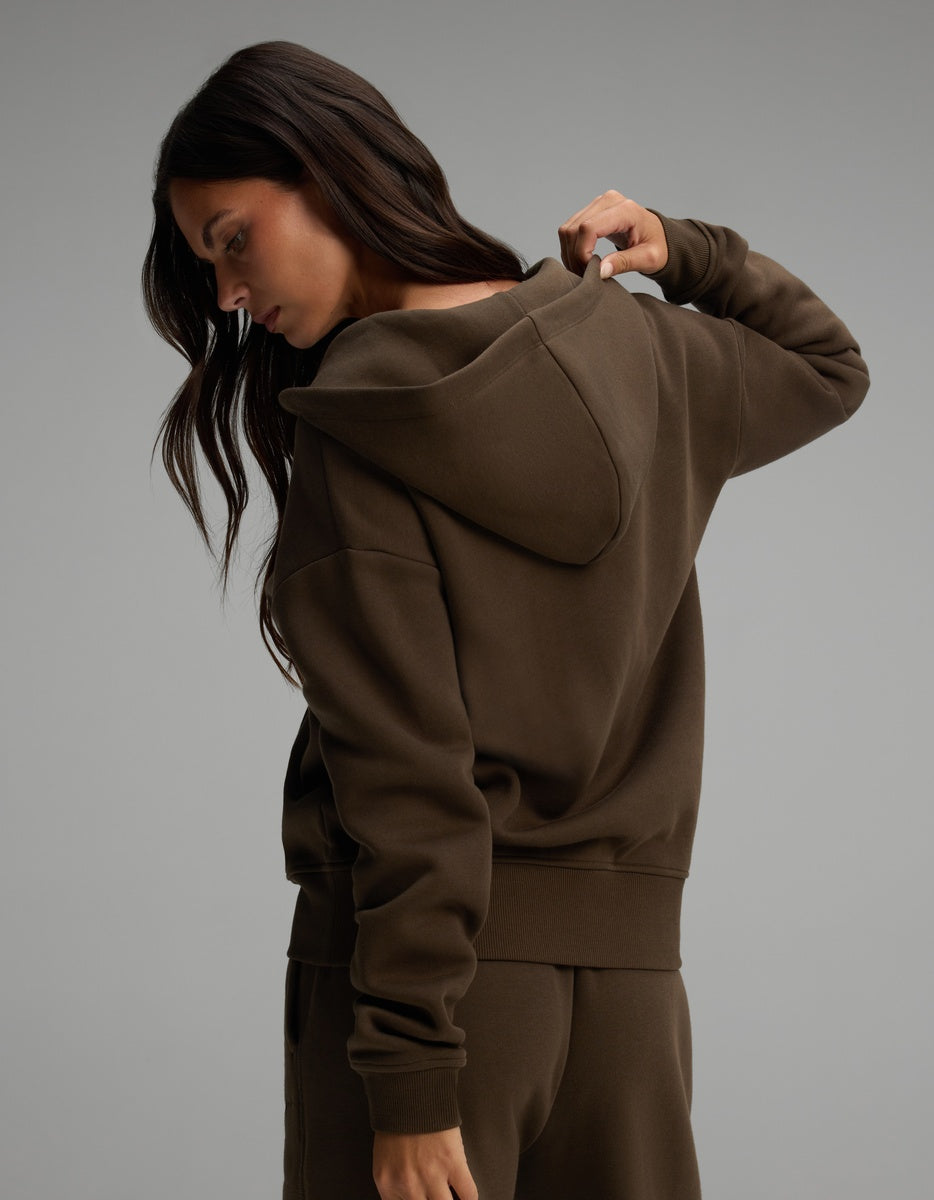 A person seen from behind, wearing a dark olive Women’s CityScape Full-Zip Hoodie with the hood up.