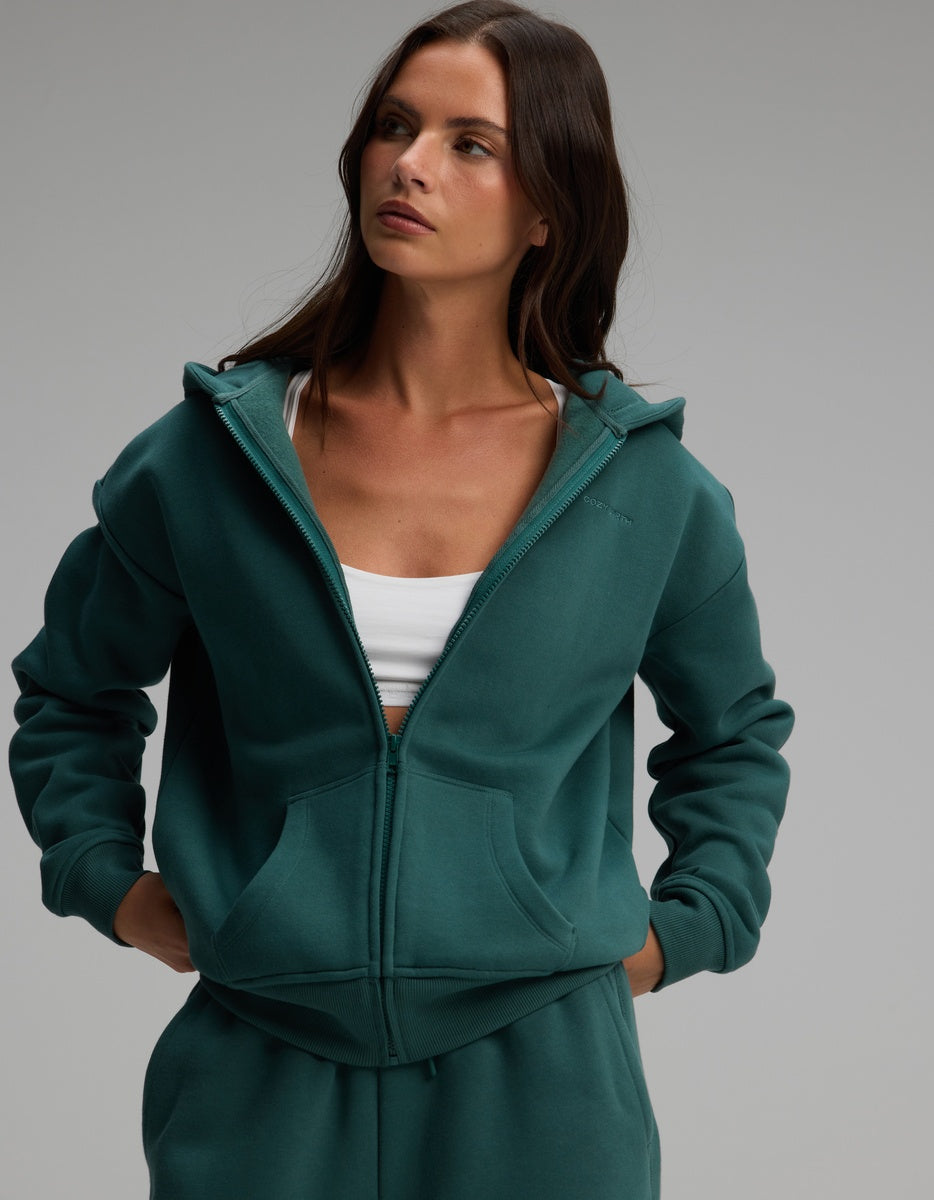 A person wearing a dark green Women’s CityScape Full-Zip Hoodie over a white top.