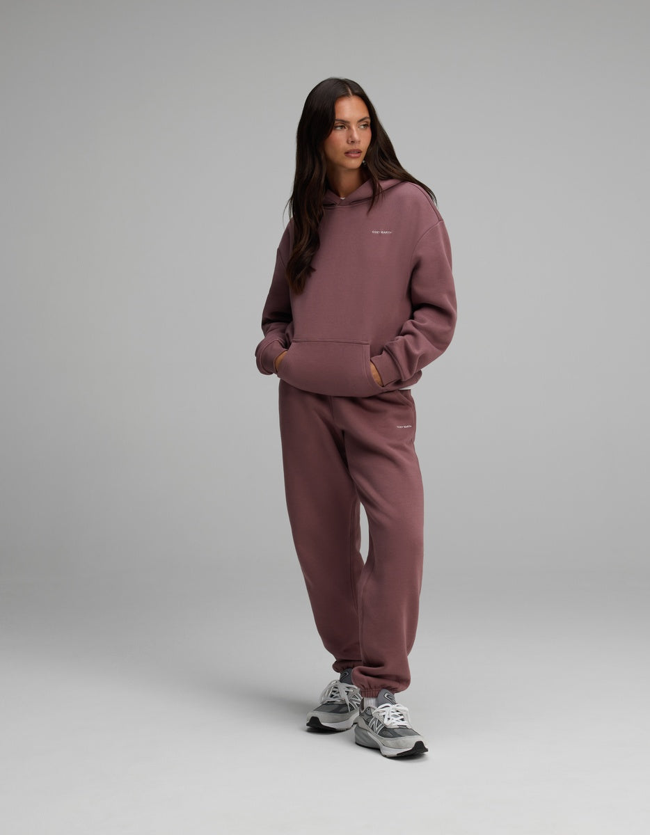 A person wearing a dusty plum-colored Cozy Earth Women’s CityScape Hoodie, matching sweatpants, and grey athletic sneakers.