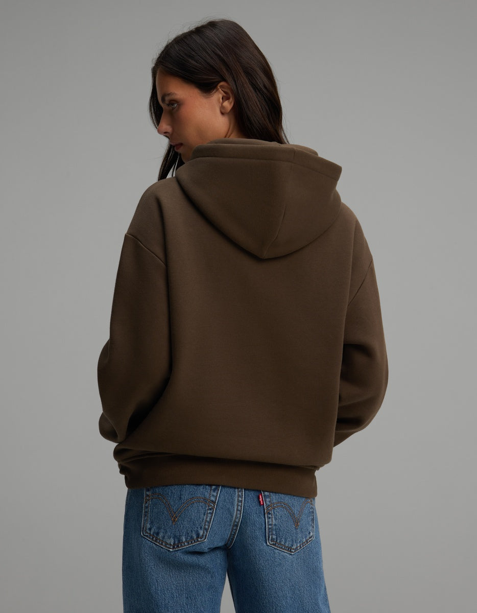 A person seen from behind wearing an oversized brown Women’s CityScape Hoodie by Cozy Earth and blue jeans.
