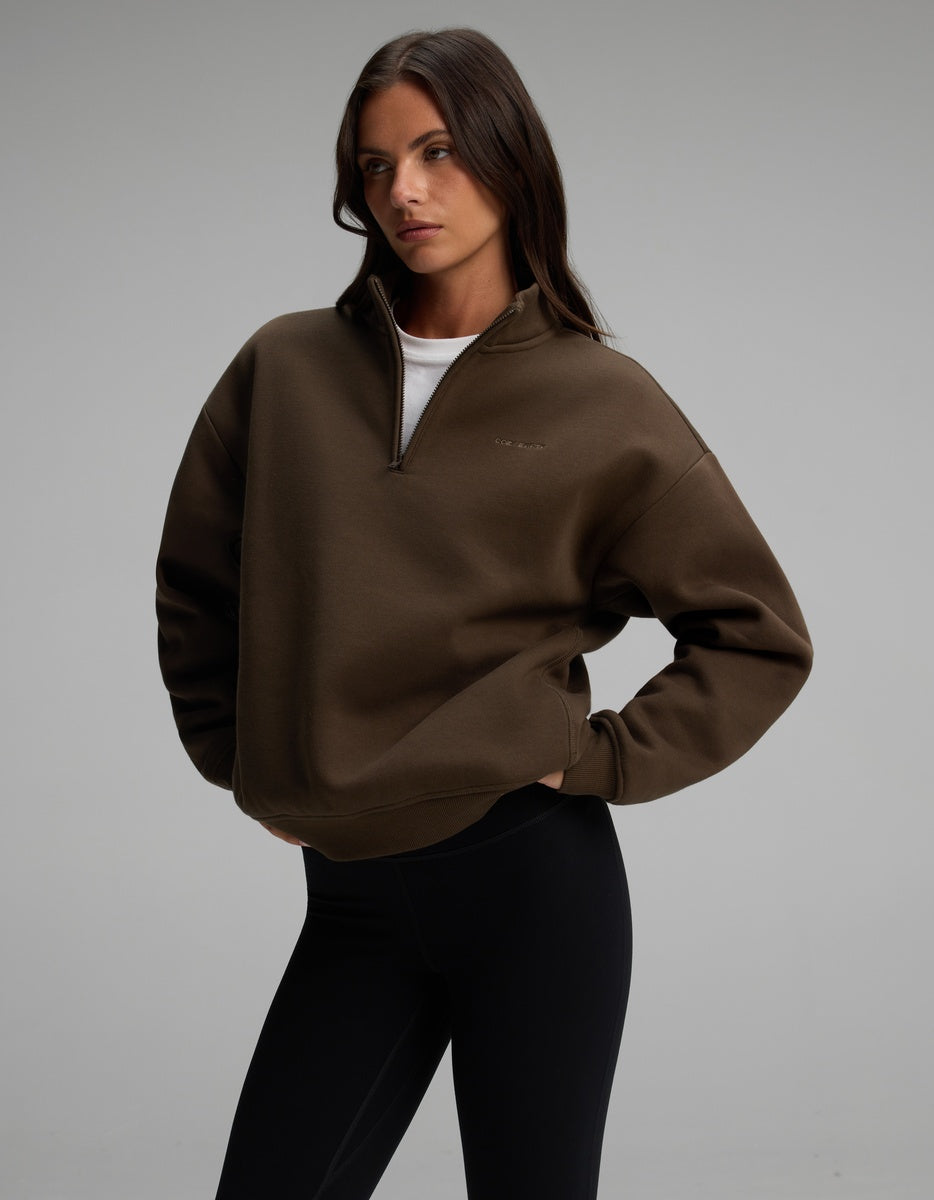 A person wearing a brown Women’s CityScape Quarter Zip and black leggings.