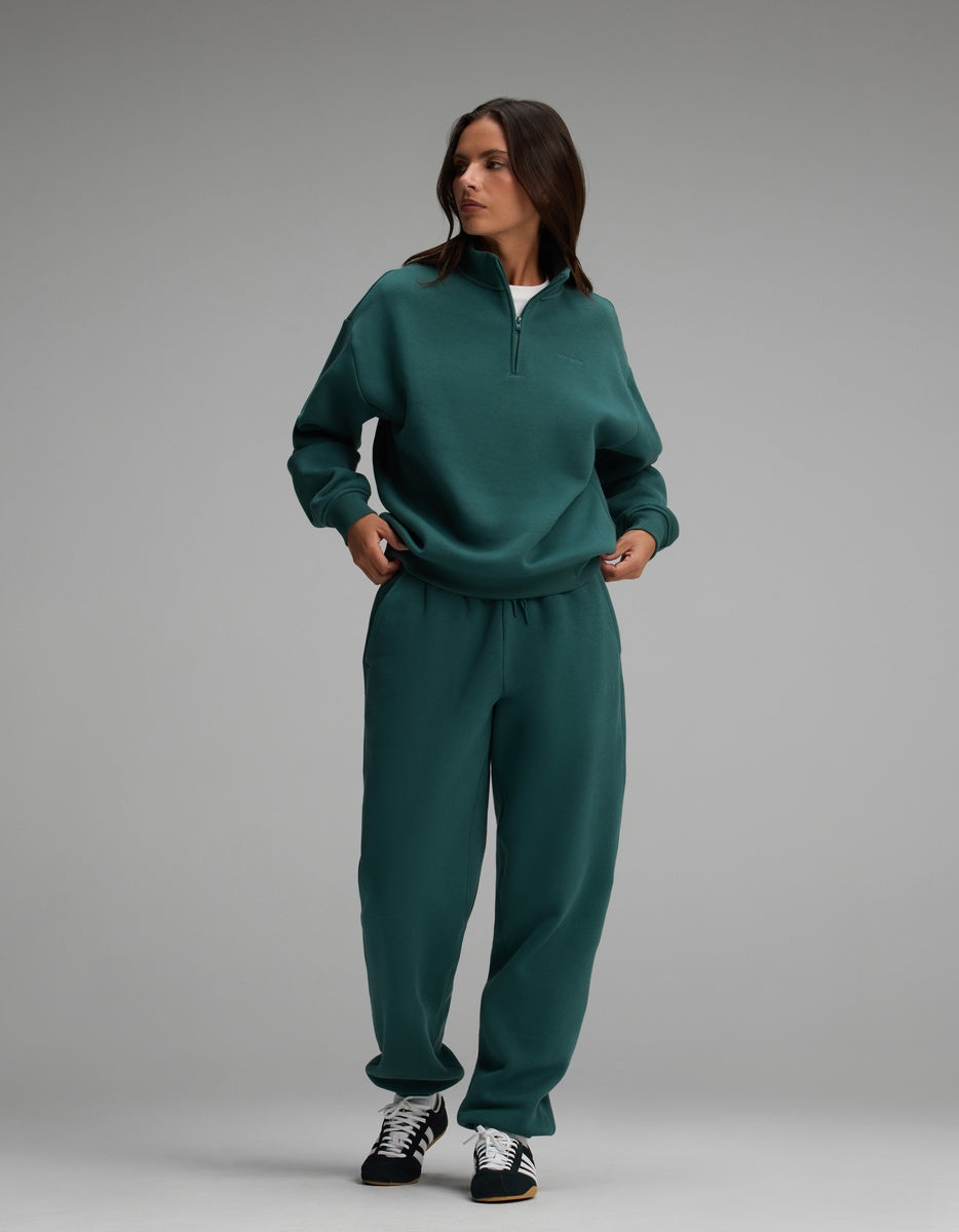 A woman wearing a dark green Cozy Earth Women’s CityScape Quarter Zip and matching sweatpants.