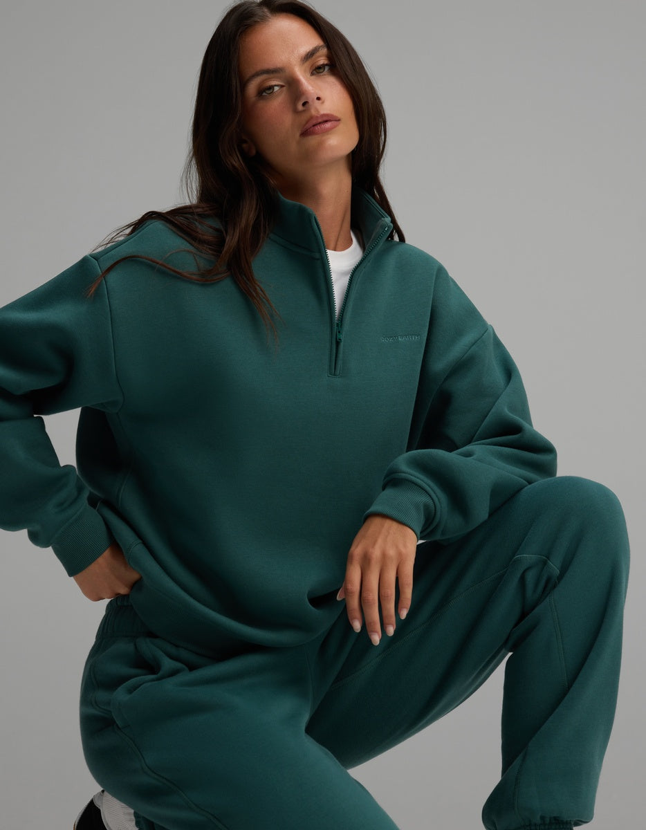 A person wearing a dark green Women’s CityScape Quarter Zip with a high collar and matching lounge pants.