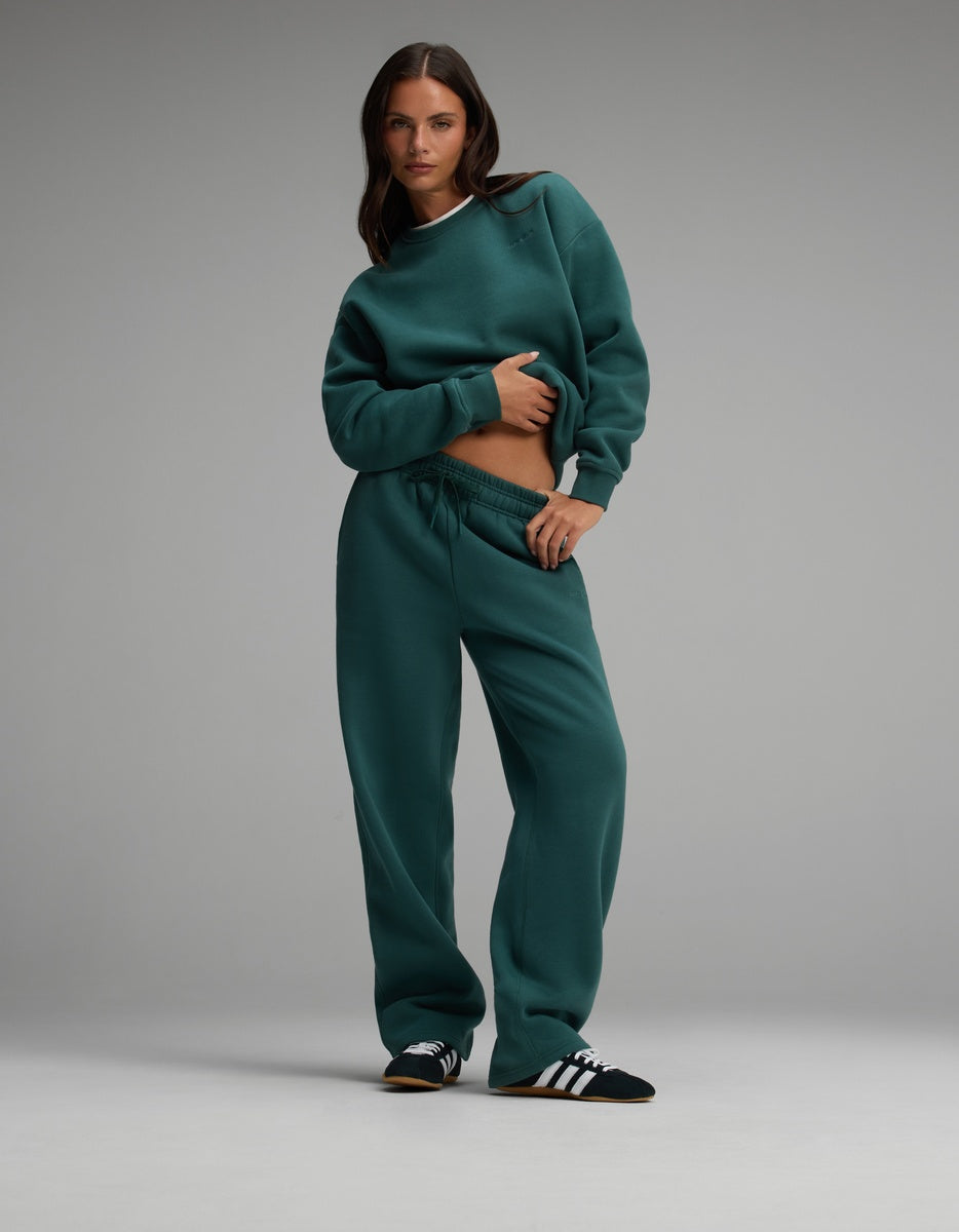 A woman wearing a dark green Cozy Earth Women’s Cityscape Crewneck & Wide Leg Pant Set consisting of a matching crewneck sweatshirt and wide-leg sweatpants.