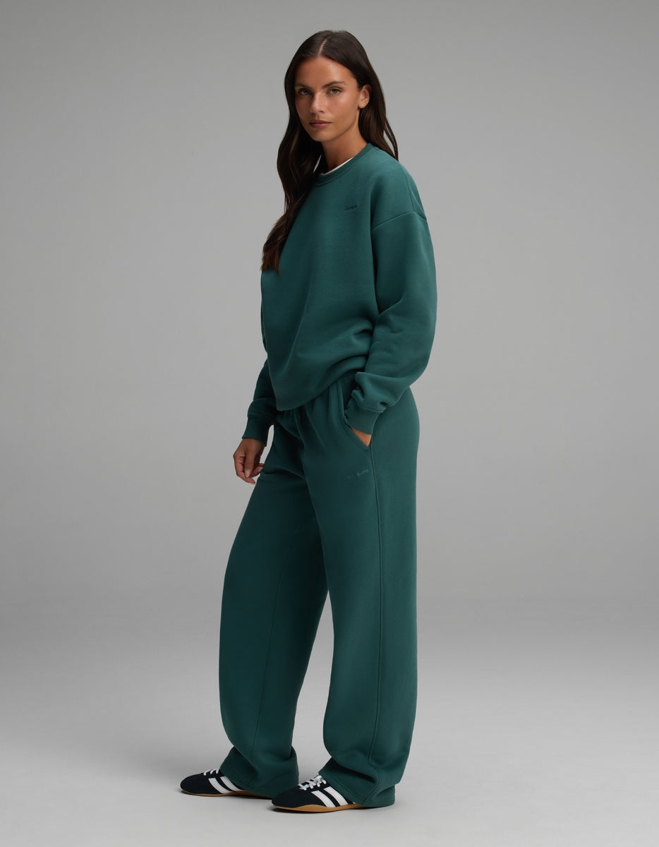 A person wearing a deep green Women’s Cityscape Crewneck & Wide Leg Pant Set paired with black and white sneakers.