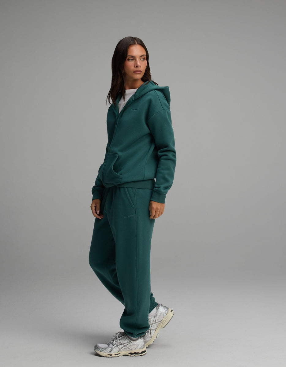 A woman wearing a dark green Cozy Earth Women’s Cityscape Full-Zip Hoodie & Sweatpant Set with white sneakers.