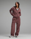 A woman wears a mauve Cozy Earth Women’s Cityscape Full-Zip Hoodie & Wide Leg Pant Set over a grey crewneck shirt, paired with grey and white sneakers.|Color:Copper Rose