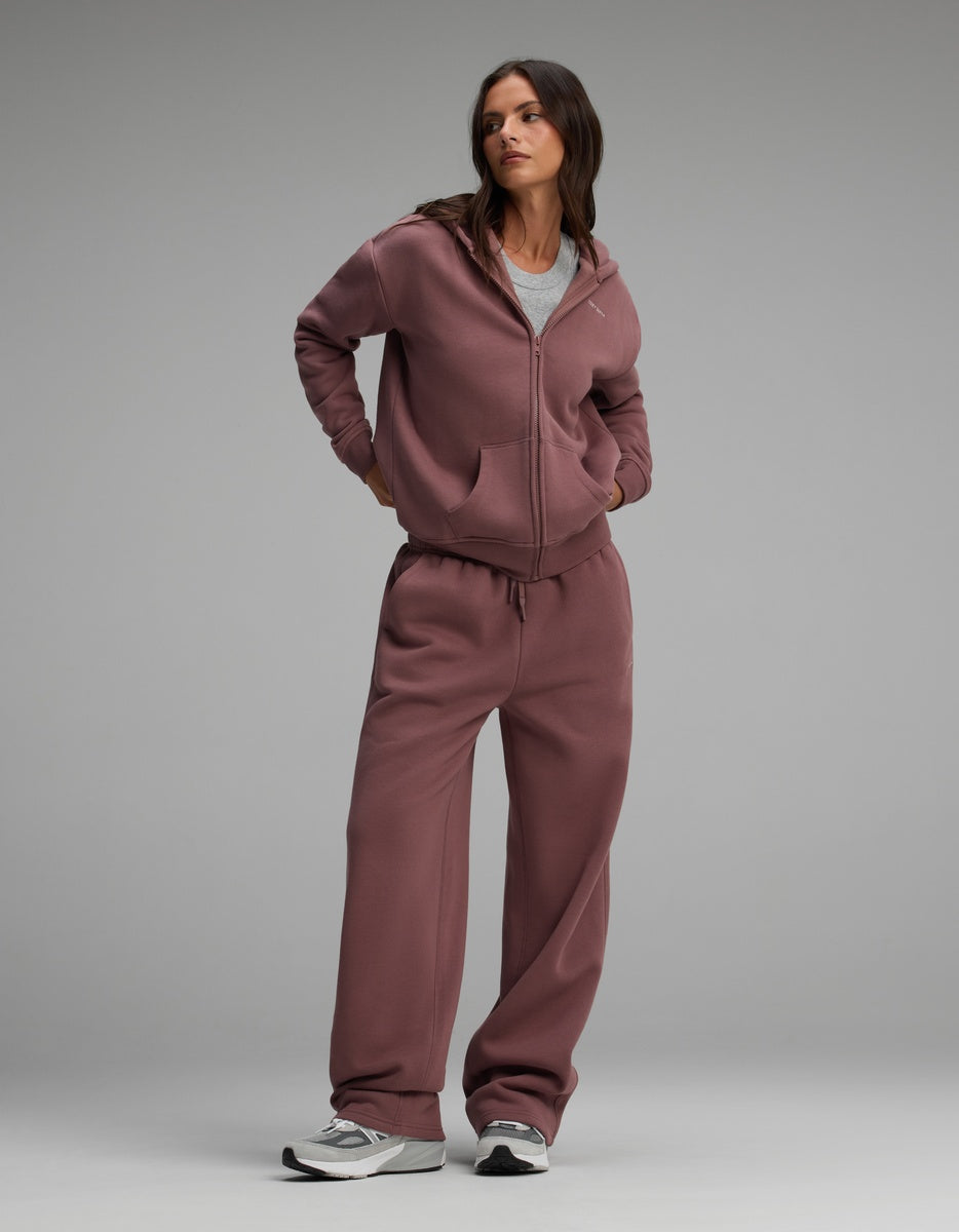 A woman wears a mauve Cozy Earth Women’s Cityscape Full-Zip Hoodie & Wide Leg Pant Set over a grey crewneck shirt, paired with grey and white sneakers.
