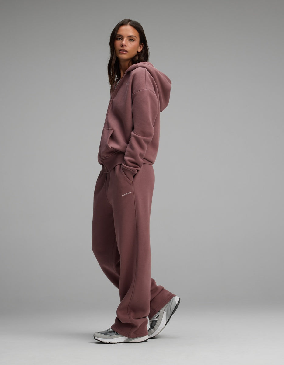 A woman wears a mauve Cozy Earth Women’s Cityscape Full-Zip Hoodie & Wide Leg Pant Set, styled with grey and white athletic sneakers.