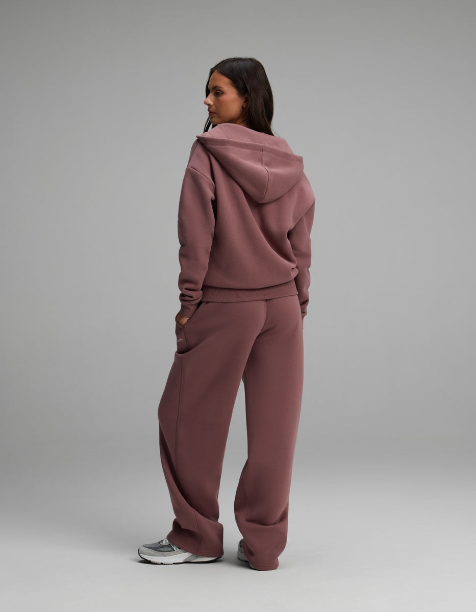 A person wearing a dusty rose Women’s Cityscape Full-Zip Hoodie & Wide Leg Pant Set, featuring a hooded sweatshirt and matching wide-leg pants.