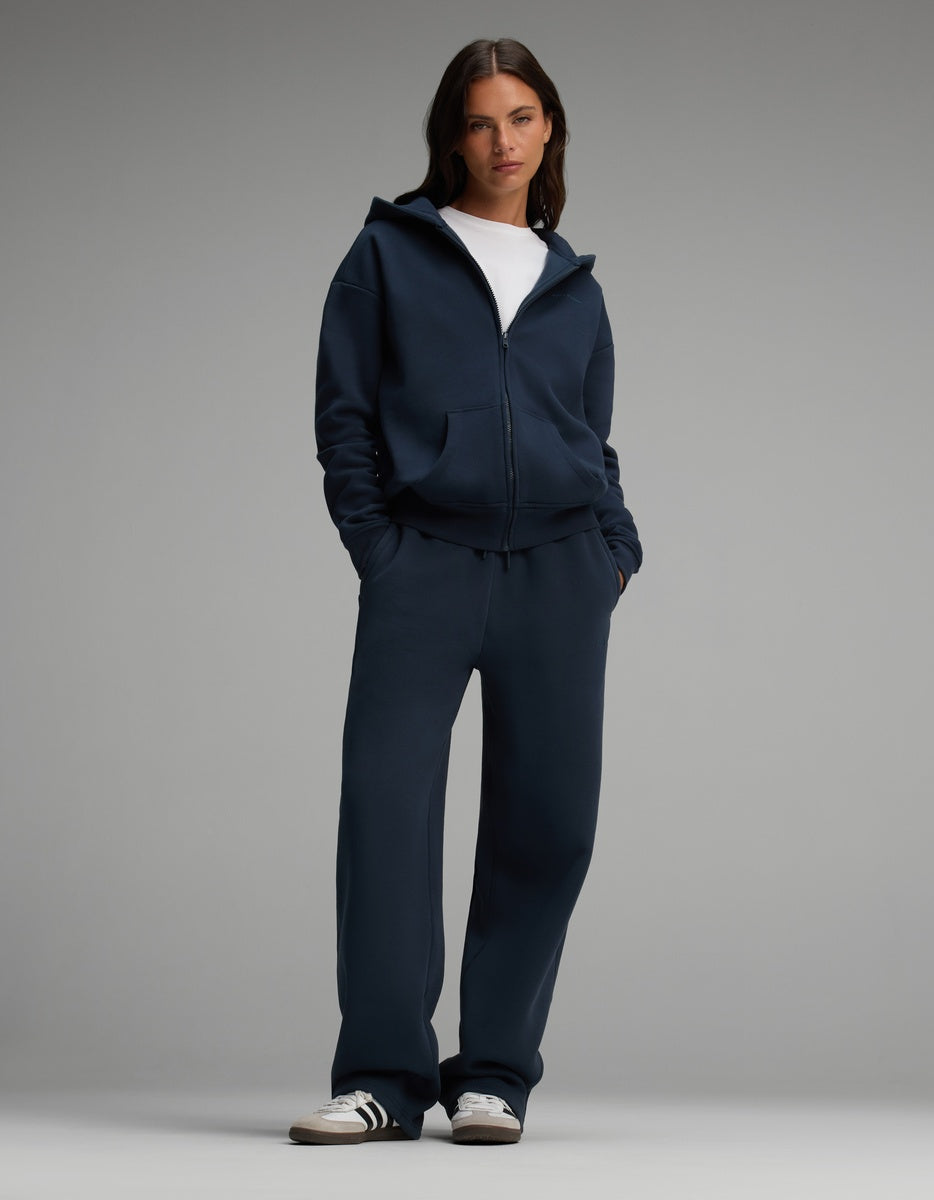 A woman wears a navy blue Cozy Earth Women’s Cityscape Full-Zip Hoodie & Wide Leg Pant Set over a white crew-neck shirt, paired with low-top sneakers.