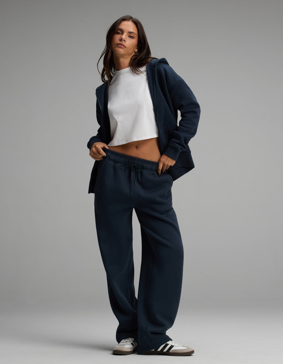 A person wearing a navy blue Cozy Earth Women’s Cityscape Full-Zip Hoodie over a white cropped t-shirt and matching wide-leg sweatpants, paired with black and white sneakers.