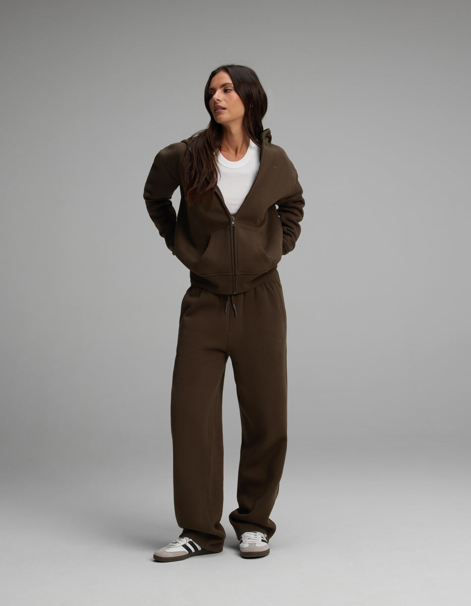 A woman wears a brown Cozy Earth Women’s Cityscape Full-Zip Hoodie & Wide Leg Pant Set over a white t-shirt, paired with casual sneakers.