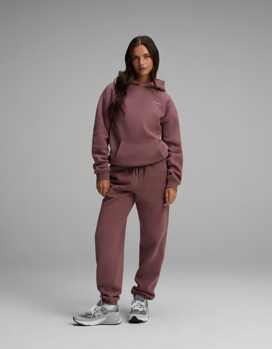 A woman wearing a mauve Women’s Cityscape Hoodie & Sweatpant Set with grey athletic sneakers.