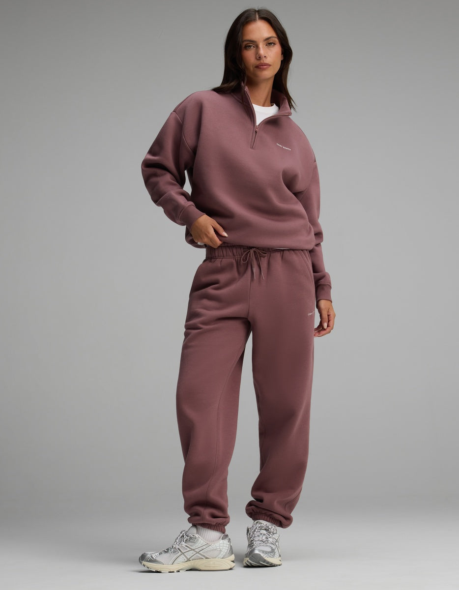 A model wearing a dark mauve Women’s Cityscape Quarter Zip & Sweatpant Set with white athletic sneakers.|Color:Copper Rose