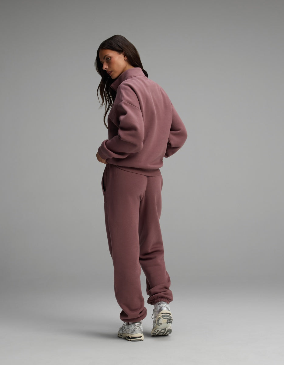 A person wearing a dusty rose Cozy Earth Women’s Cityscape Quarter Zip & Sweatpant Set with cuffed hems and athletic sneakers.