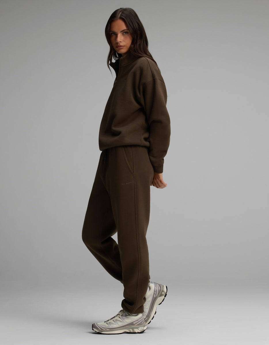 A person wearing a dark brown Cozy Earth Women’s Cityscape Quarter Zip & Sweatpant Set and gray athletic sneakers.