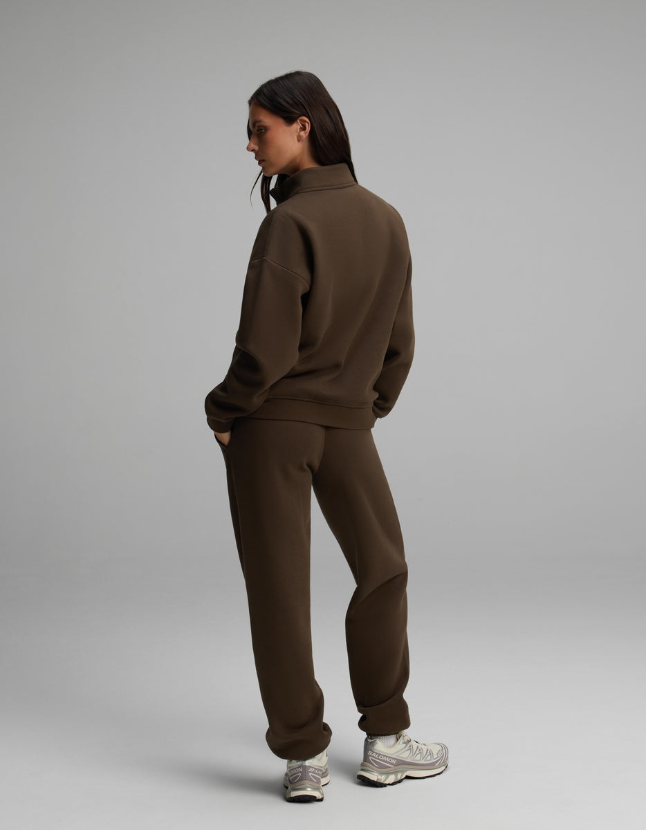 A woman wearing a dark brown Cozy Earth Women’s Cityscape Quarter Zip & Sweatpant Set with grey and white sneakers.
