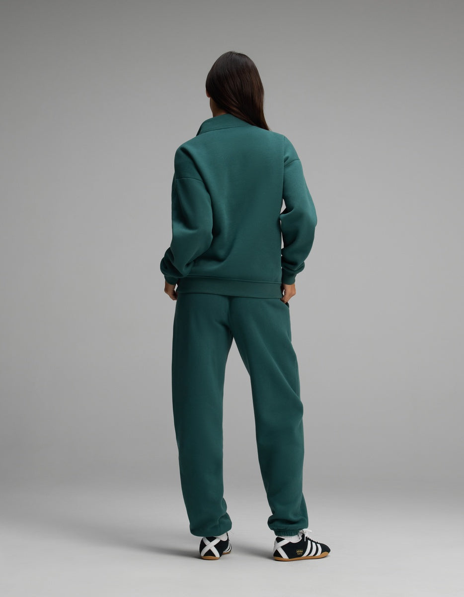 A person seen from behind wears a forest green Cozy Earth Women’s Cityscape Quarter Zip & Sweatpant Set with black and white sneakers.