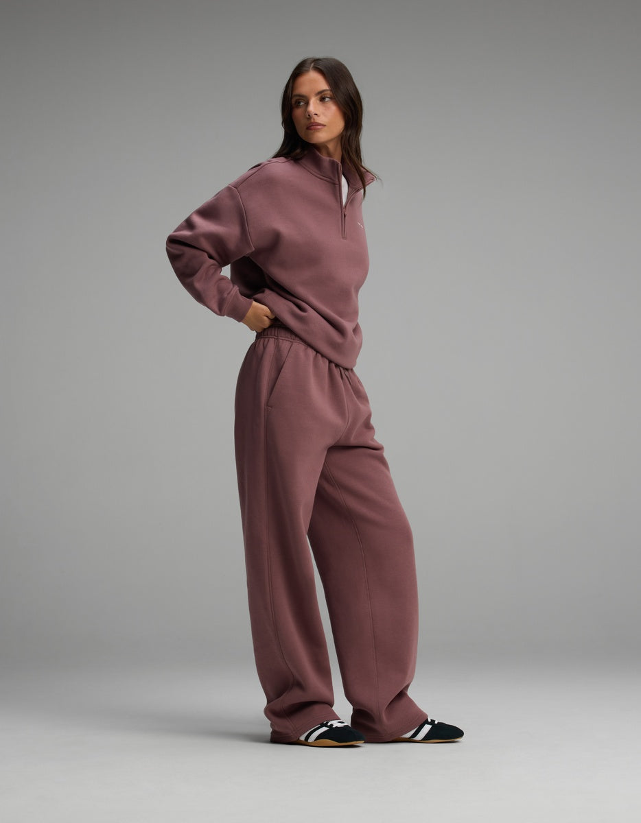 A person wearing a dusty rose-colored Women’s Cityscape Quarter Zip & Wide Leg Pant Set consisting of a quarter-zip sweatshirt and matching wide-leg sweatpants.