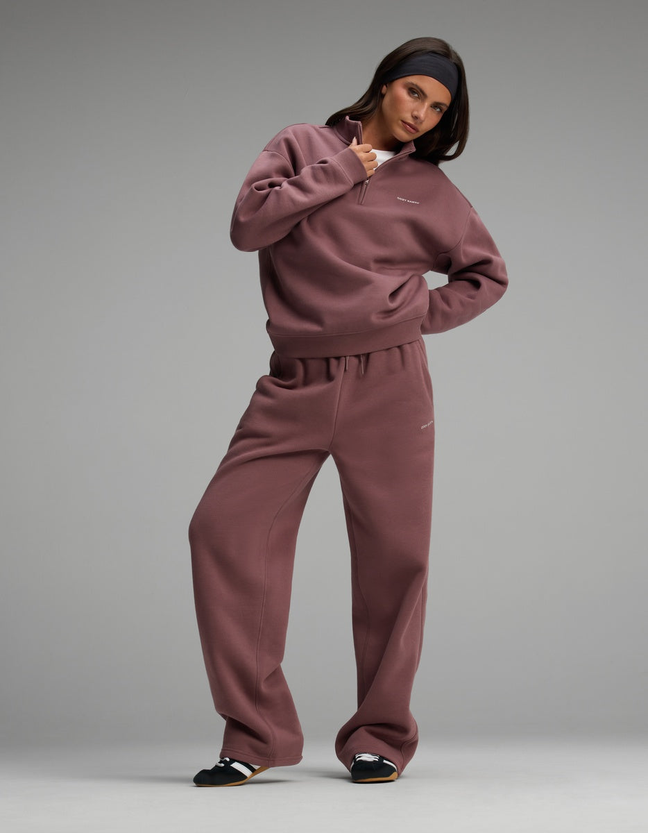 A person wearing a dusty purple Women’s Cityscape Quarter Zip & Wide Leg Pant Set consisting of a quarter-zip sweatshirt and matching wide-leg sweatpants.