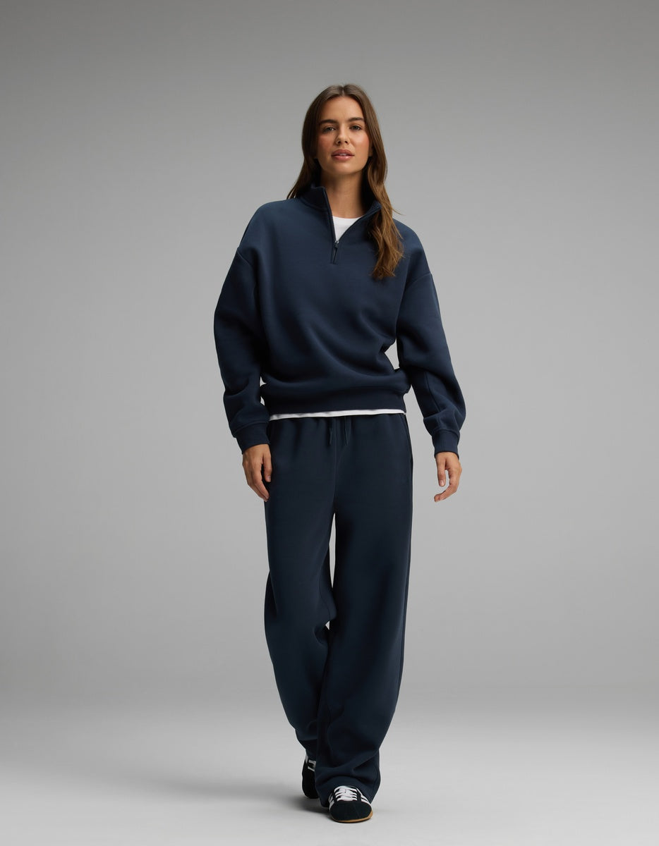 A woman wearing a navy blue Cozy Earth Women’s Cityscape Quarter Zip & Wide Leg Pant Set, consisting of a quarter-zip sweatshirt and matching wide-leg sweatpants.