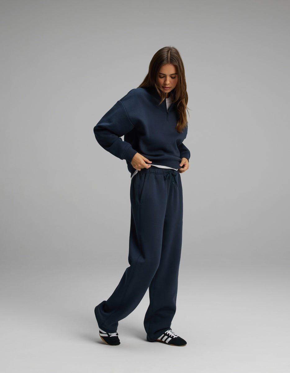 A person wearing a dark blue Cozy Earth Women’s Cityscape Quarter Zip & Wide Leg Pant Set consisting of a long-sleeve quarter-zip pullover and matching wide-leg sweatpants.