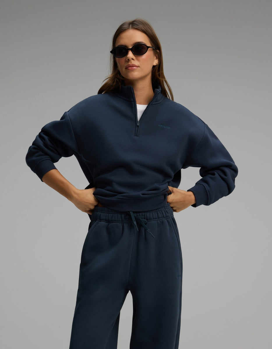 A person wearing a navy blue Cozy Earth Women’s Cityscape Quarter Zip & Wide Leg Pant Set consisting of a quarter-zip sweatshirt and matching wide-leg sweatpants.