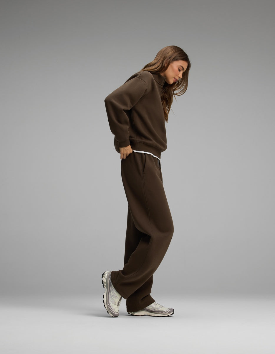 A woman wearing a brown Cozy Earth Women’s Cityscape Quarter Zip & Wide Leg Pant Set, featuring a quarter-zip sweatshirt, matching wide-leg sweatpants, and athletic sneakers.