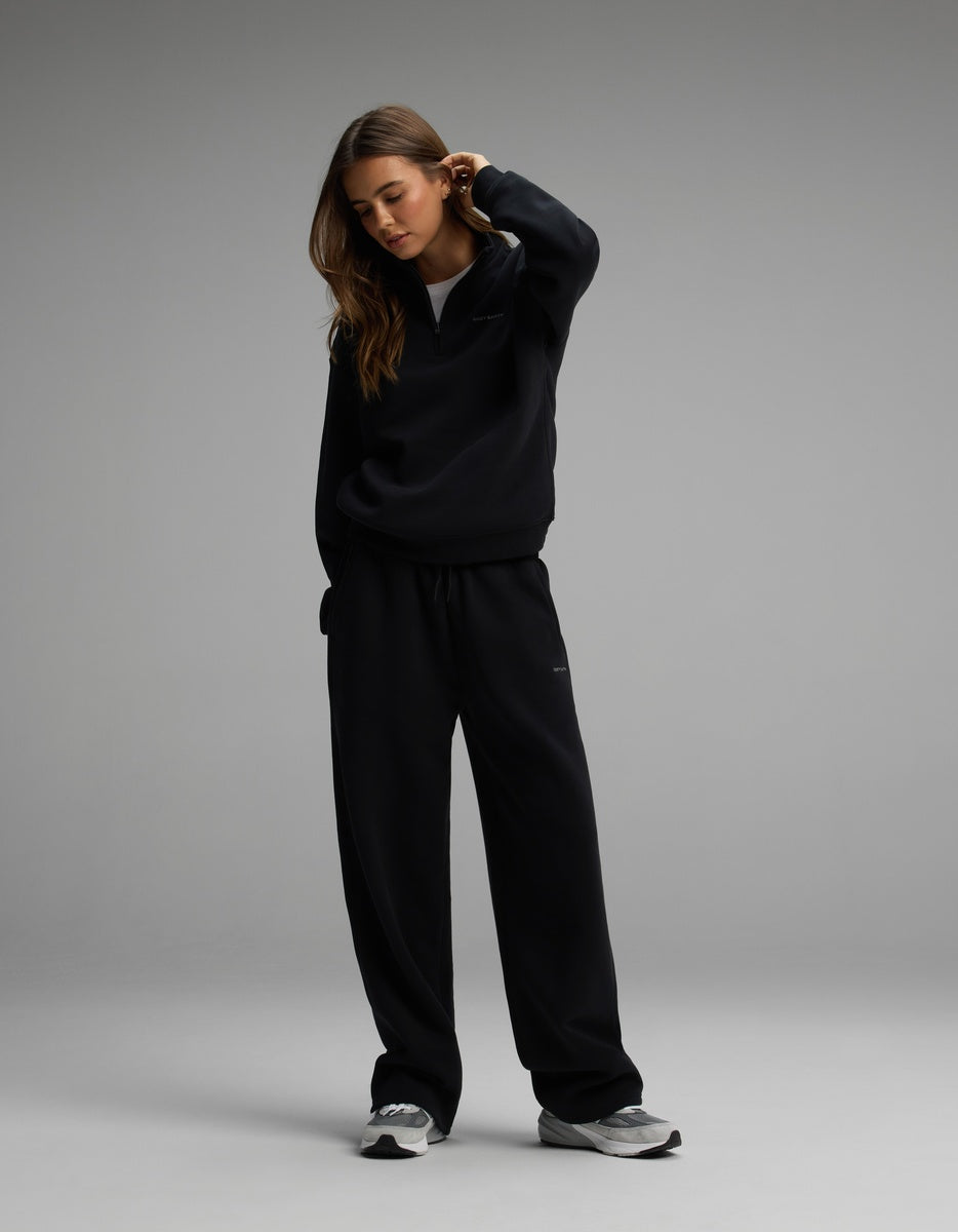 A person wearing a black Cozy Earth Women’s Cityscape Quarter Zip & Wide Leg Pant Set with matching wide-leg lounge pants and grey athletic shoes.
