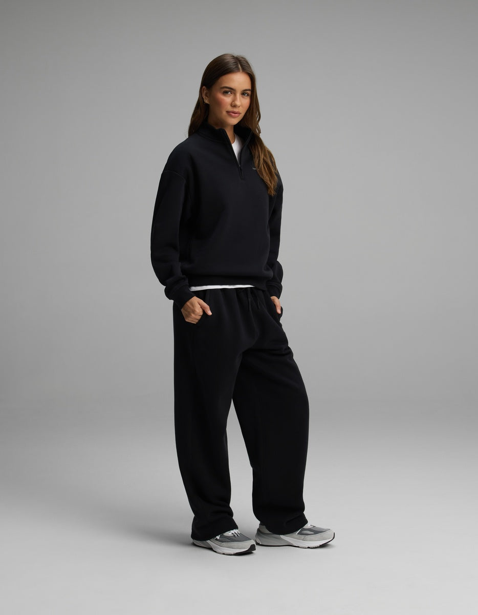 A woman wearing a black Women’s Cityscape Quarter Zip & Wide Leg Pant Set, consisting of a quarter-zip sweatshirt and matching wide-leg sweatpants.