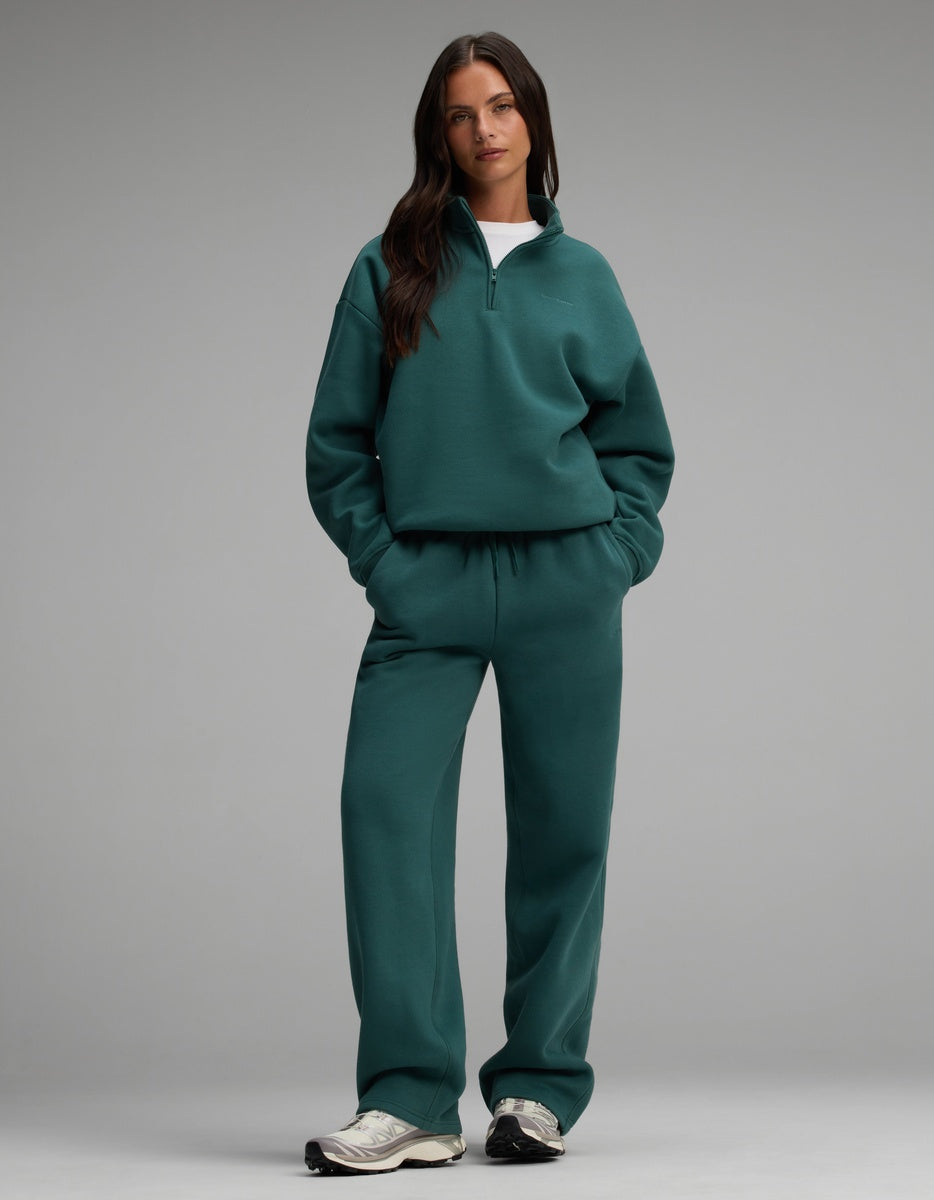 A woman wearing a dark teal Women’s Cityscape Quarter Zip & Wide Leg Pant Set paired with grey athletic sneakers.