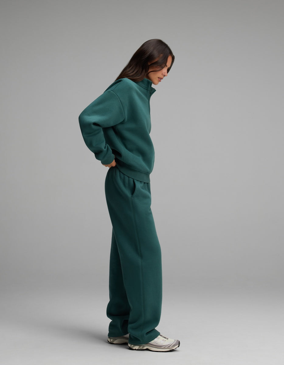 A person wears a dark green Cozy Earth Women’s Cityscape Quarter Zip & Wide Leg Pant Set with matching wide-leg sweatpants and athletic sneakers.