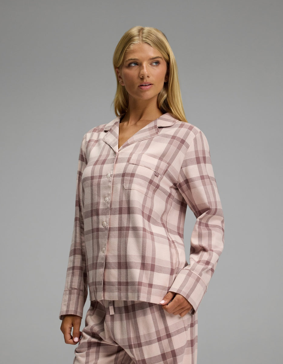 A woman wears a Cozy Earth Women’s Farmhouse Long Sleeve Pajama Top, featuring a pink and brown plaid pattern, a notched collar, and long sleeves.