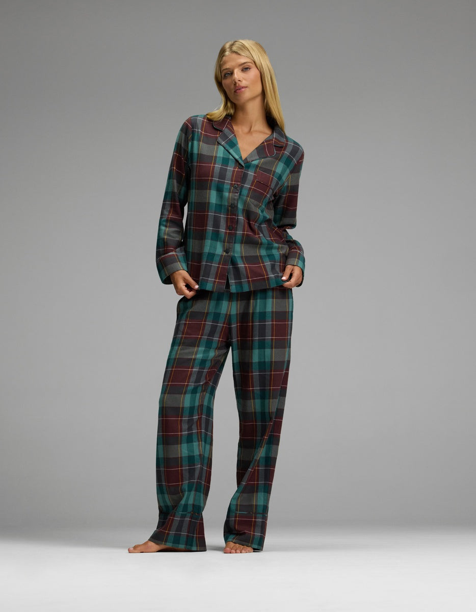 A woman modeling the Cozy Earth Women’s Farmhouse Long Sleeve Pajama Top and matching pants in a dark green, maroon, and grey plaid pattern.