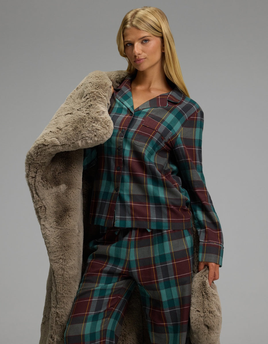 A woman wearing a Cozy Earth Women’s Farmhouse Long Sleeve Pajama Top in a teal, maroon, and yellow plaid pattern, draped in a fuzzy tan robe.