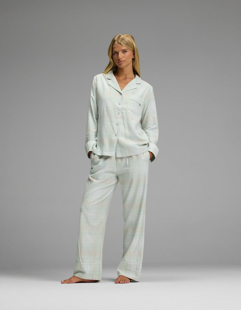 A woman wearing a light-colored Women’s Farmhouse Long Sleeve Pajama Top and matching pants with a subtle grid pattern.
