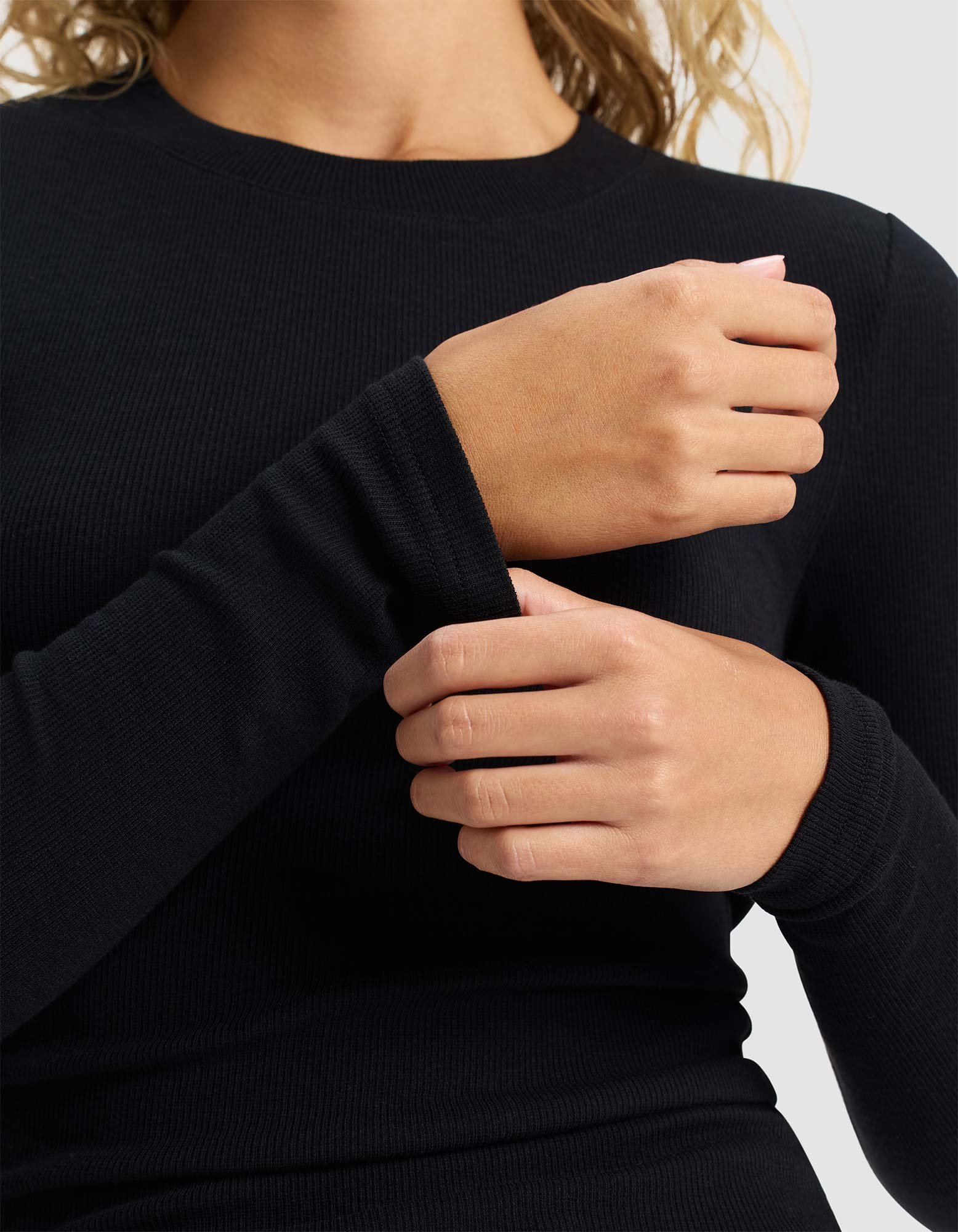 A person wearing Cozy Earth's Women's Fine Ribbed Long Sleeve Tee in black adjusts their sleeve; only the torso and hands are visible.
