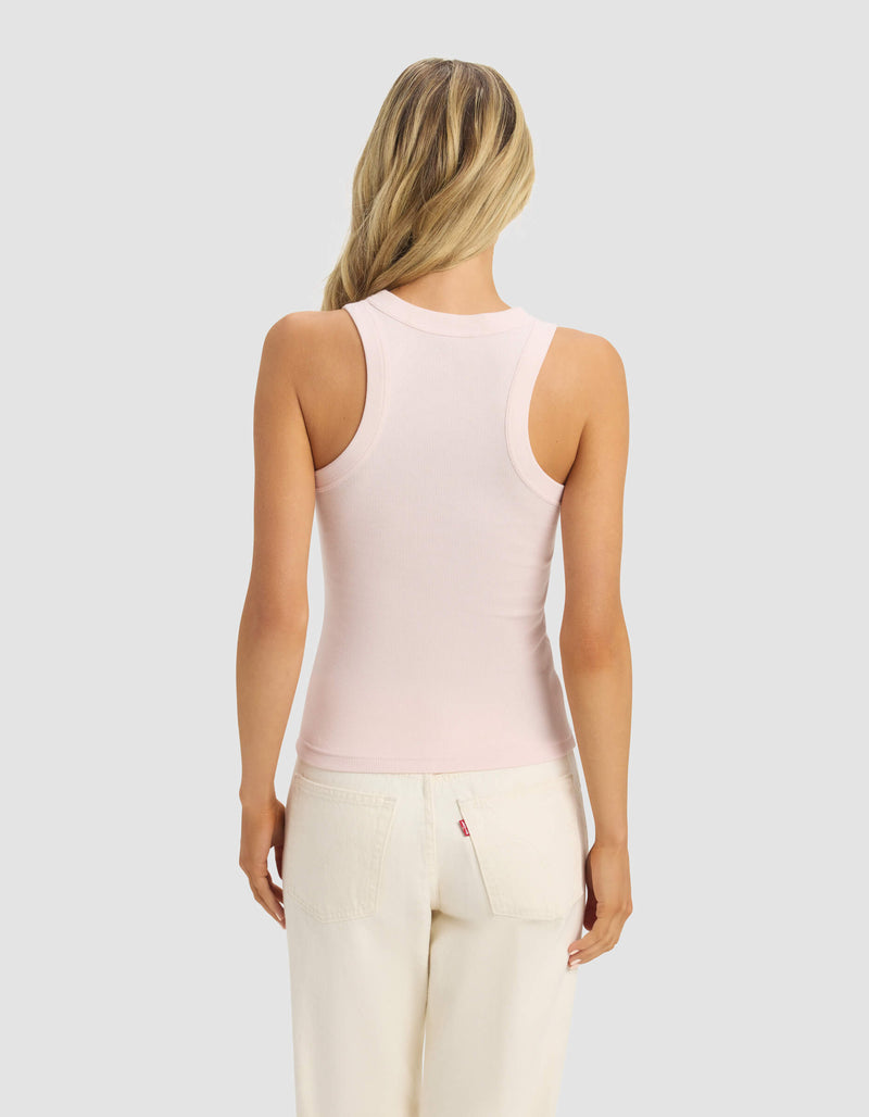 A woman with long blonde hair, seen from the back, wears the Cozy Earth Women's Fine Ribbed Tank in light pink and off-white pants, standing against a plain light gray background.