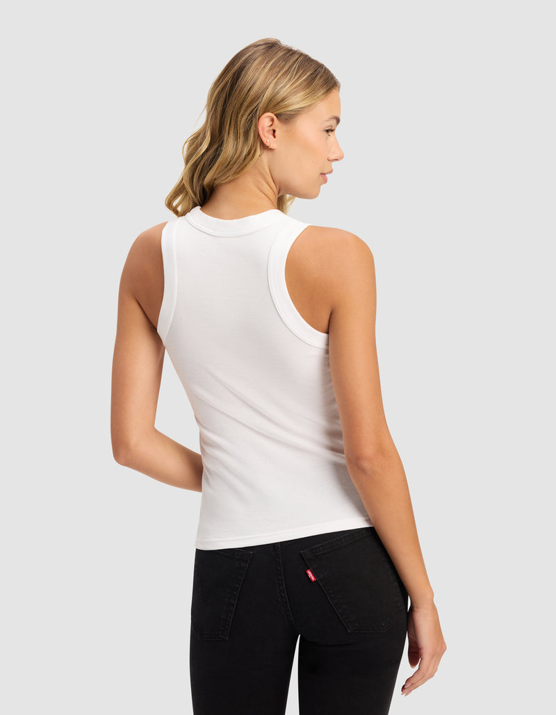 A woman with blonde wavy hair stands with her back to the camera, wearing Cozy Earth's Women's Fine Ribbed Tank in white and black jeans, set against a light gray background.