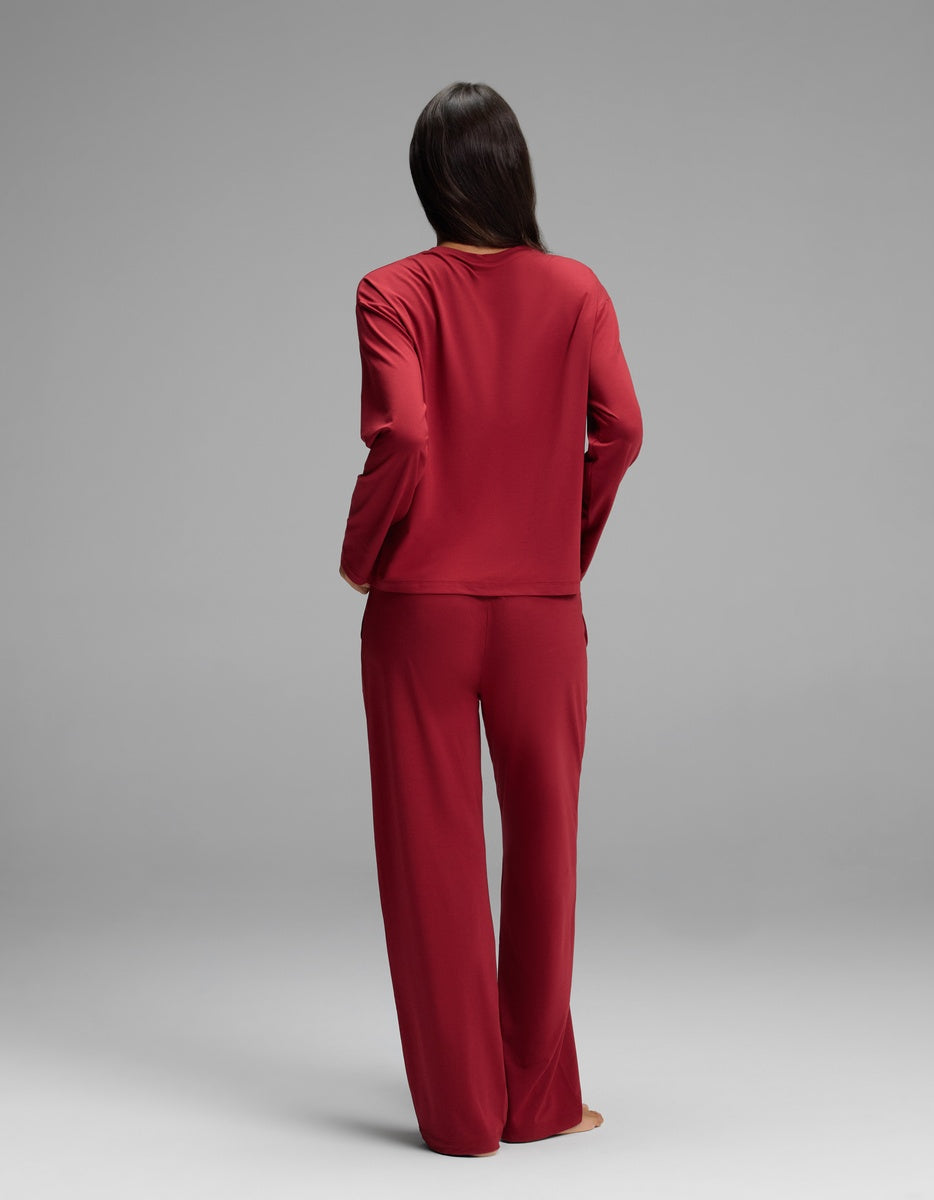 Back view of a person wearing a dark red Women’s First Layer Long Sleeve Sleep Tee & Pajama Pant Set with a long-sleeve top and wide-leg pants.