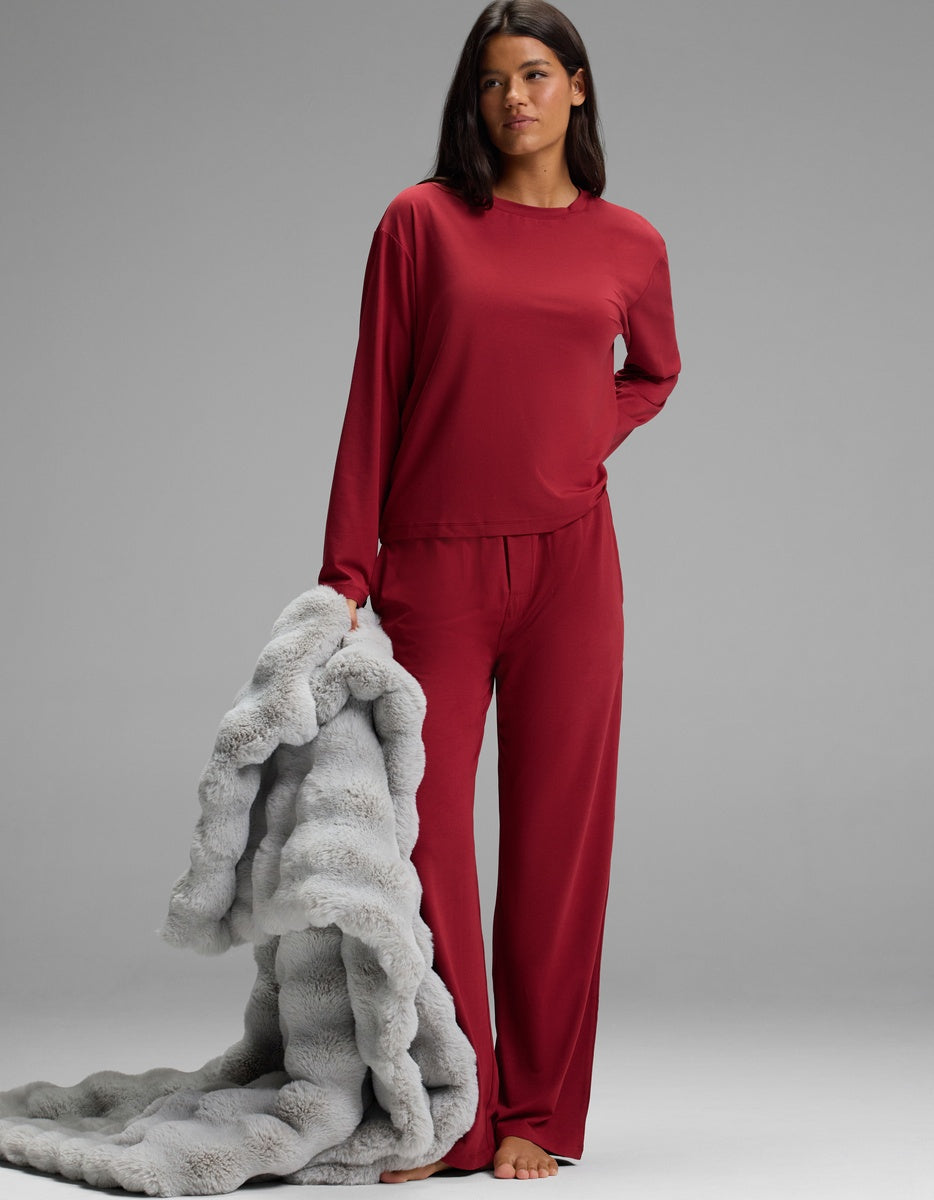 A person wearing a red Women’s First Layer Long Sleeve Sleep Tee & Pajama Pant Set and holding a textured gray blanket.