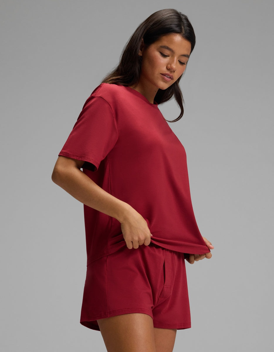 A woman wearing a dark red Women’s First Layer Pajama Short Sleeve Tee & Boxer Short Set featuring a matching short-sleeve crewneck tee and pajama shorts.