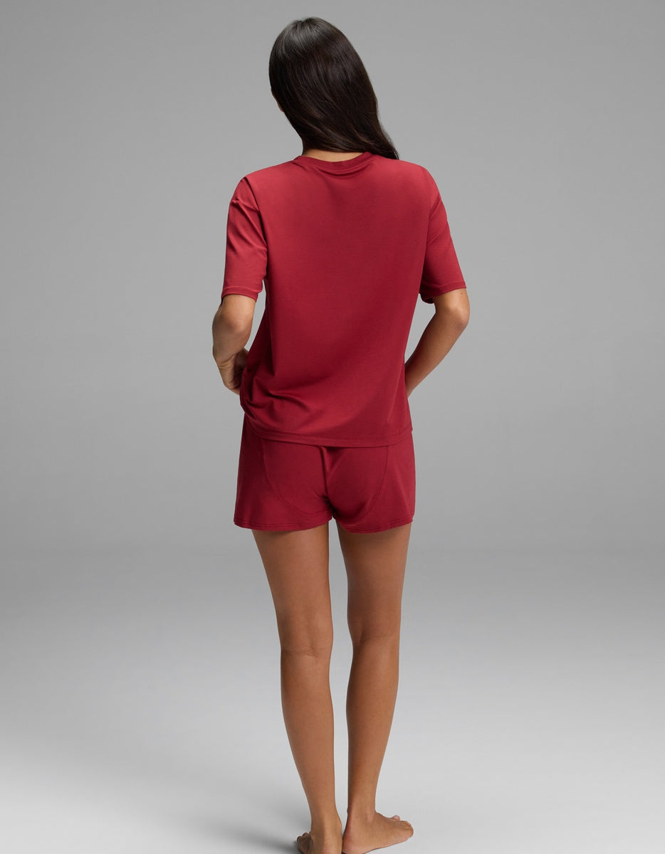 A person seen from behind wears a burgundy Women’s First Layer Pajama Short Sleeve Tee & Boxer Short Set featuring a short-sleeve top and matching shorts.