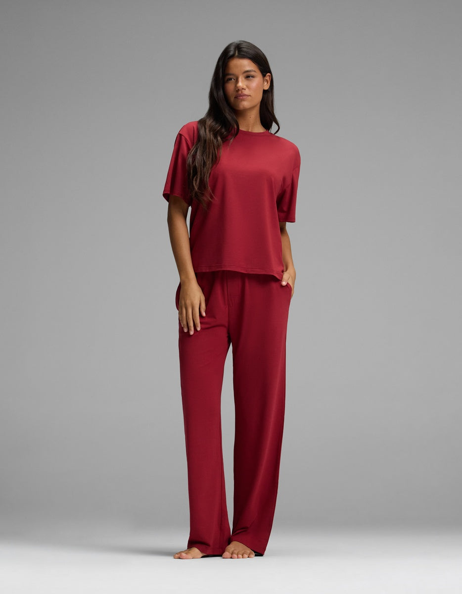 A woman wearing a deep red Women’s First Layer Pajama Short Sleeve Tee & Pajama Pant Set with a matching short-sleeve top and full-length lounge pants.