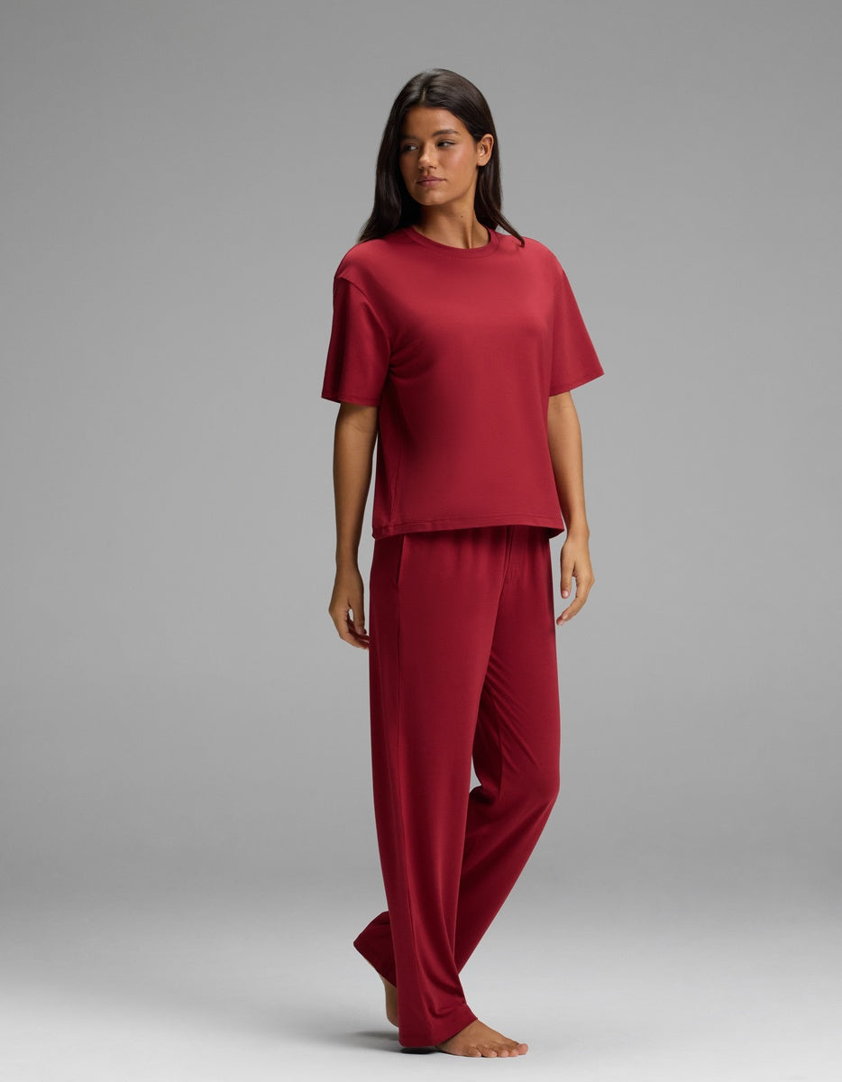 A person wearing a dark red Women’s First Layer Pajama Short Sleeve Tee & Pajama Pant Set, consisting of a short-sleeved crew neck t-shirt and matching lounge pants.